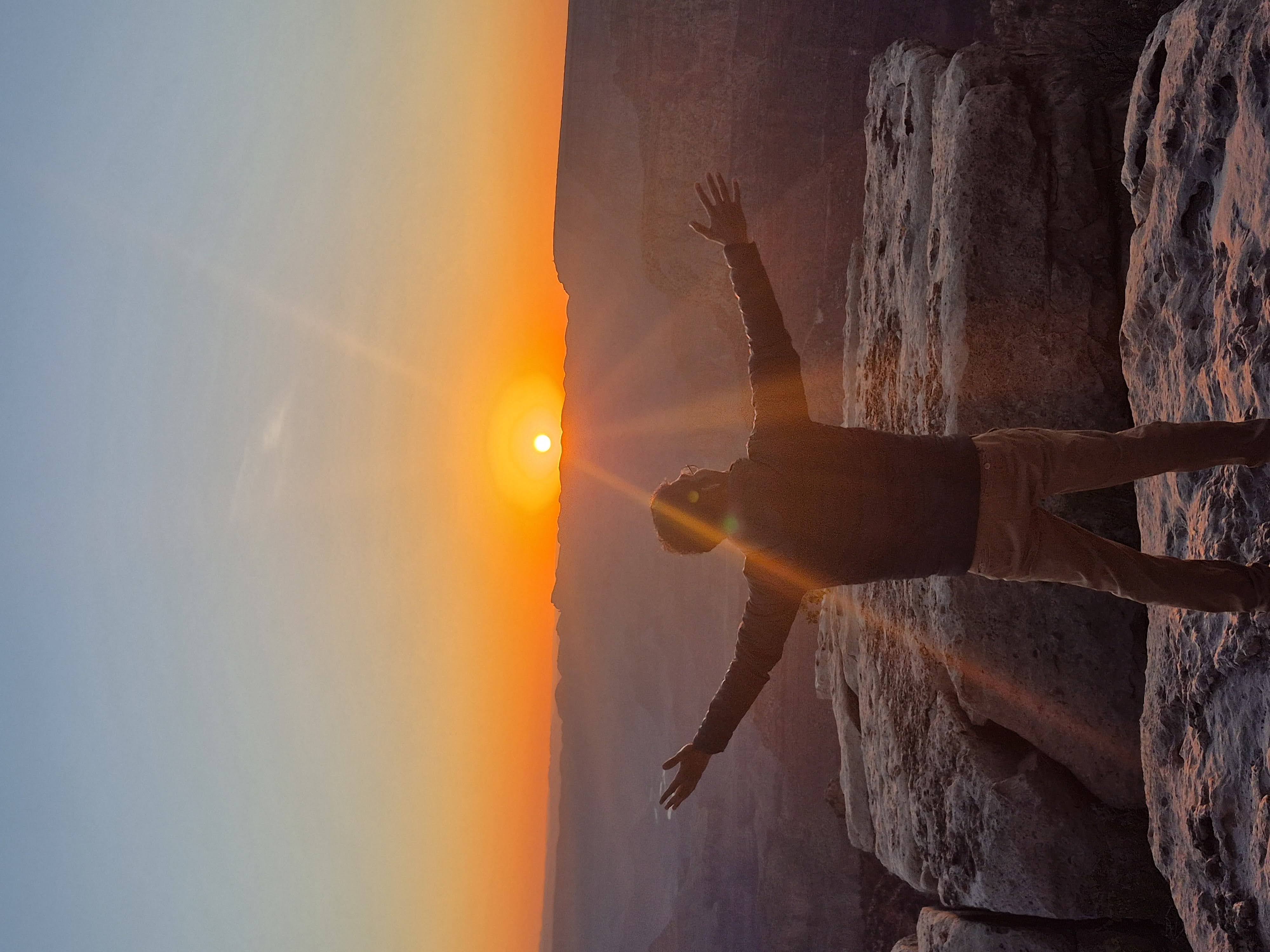 Aldrin standing on the rocks at the Grand Canyon's edge, arms spread wide, silhouetted against the rising sun