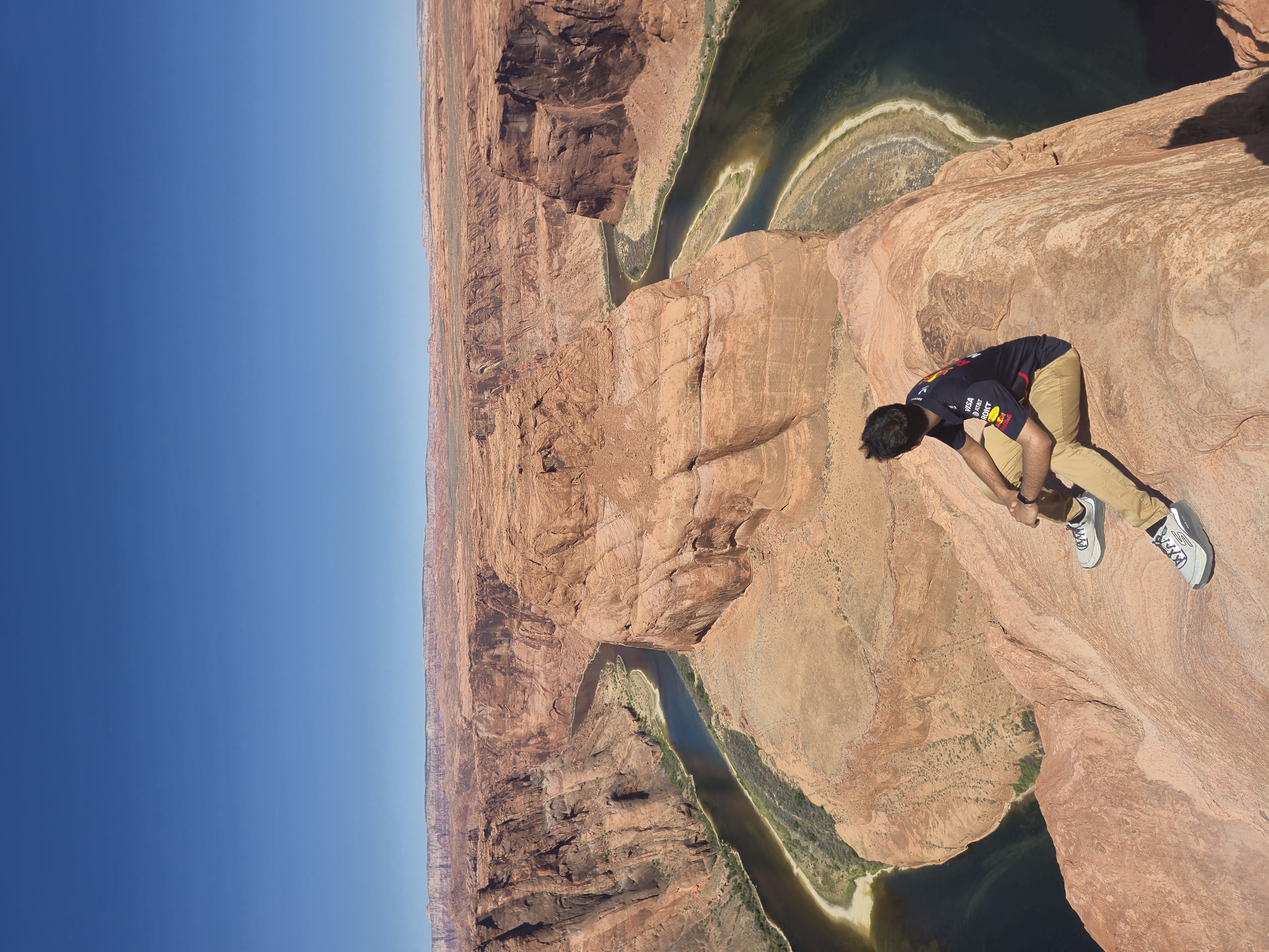 Aldrin perched on the rock ledge above Horseshoe Bend, the Colorado River curving in a deep U around a sandstone butte far below
