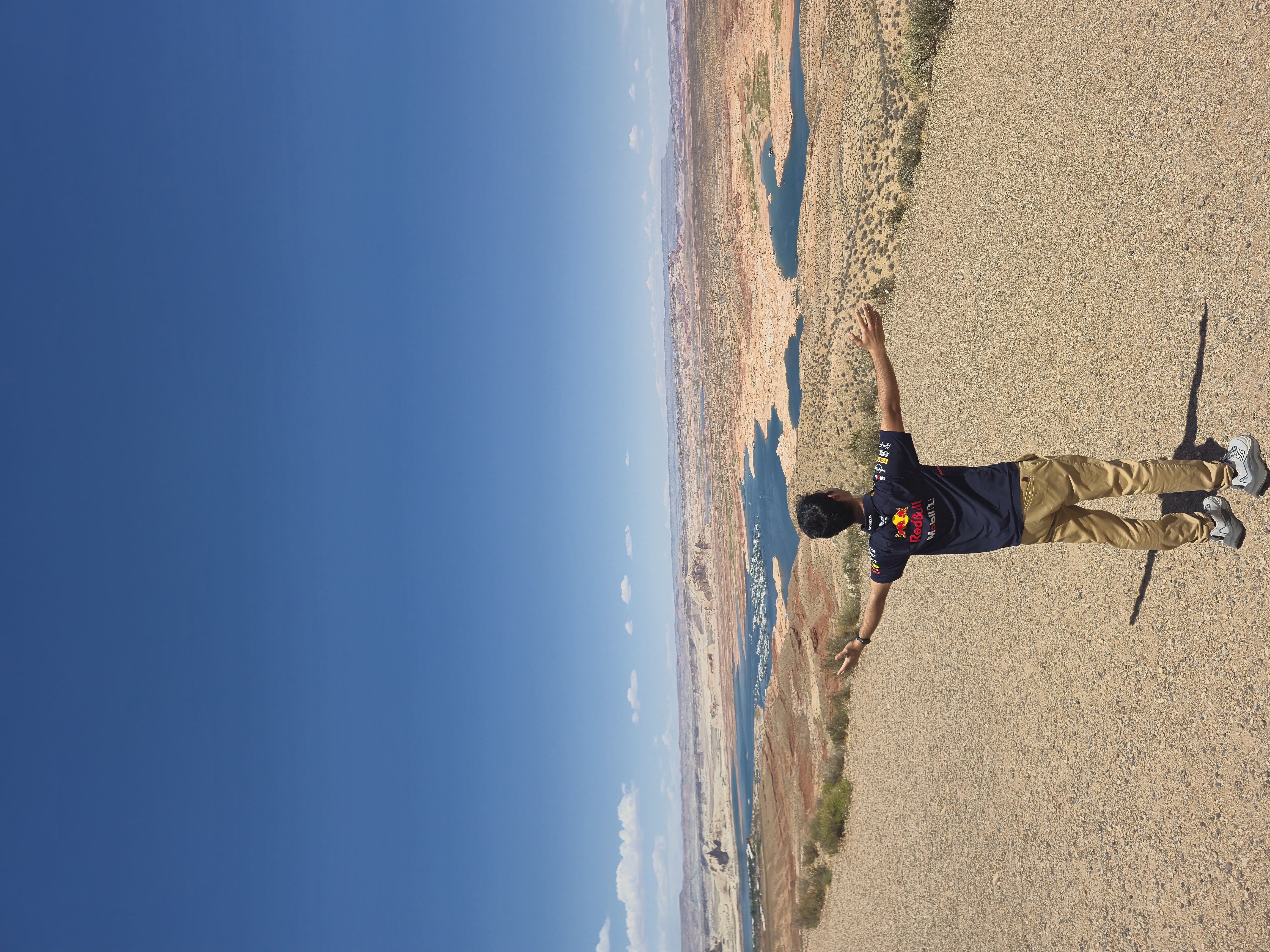Aldrin with arms outstretched on the sandy shore of Lake Powell, blue water and pale desert hills stretching into the distance under a deep blue sky