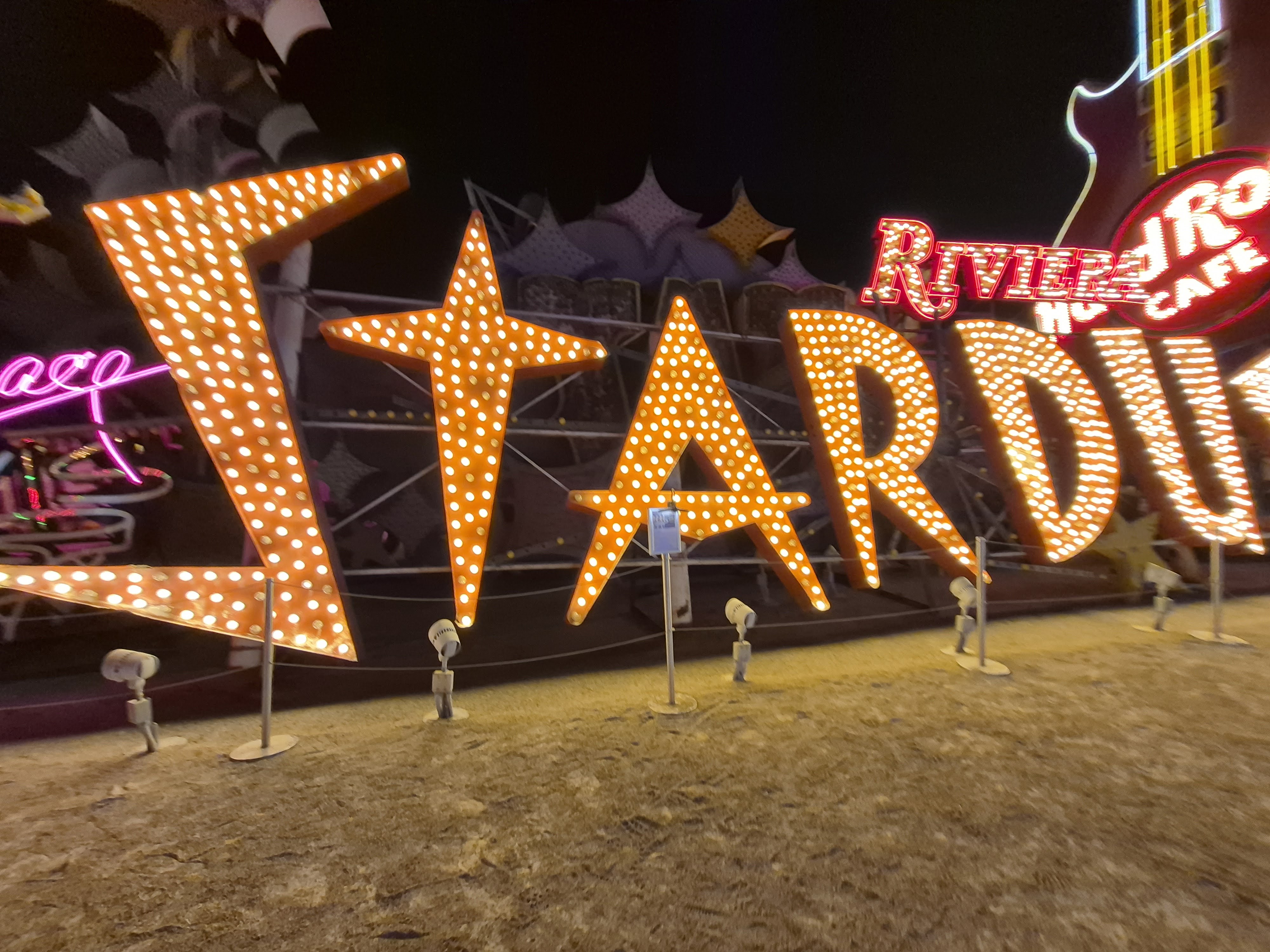 The restored, brightly-lit Stardust casino sign at night in the Neon Museum boneyard, with other old neon signs around it